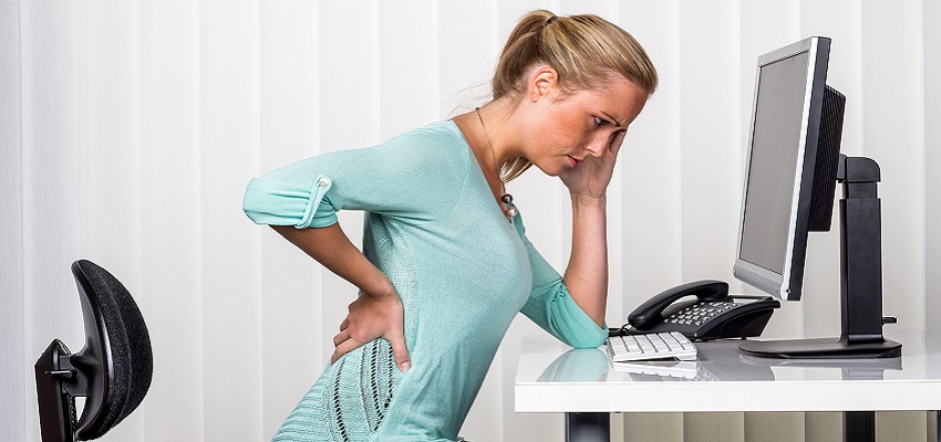 a woman sitting at a desk and has pain in the back. symbol photo for proper posture at work in the office.