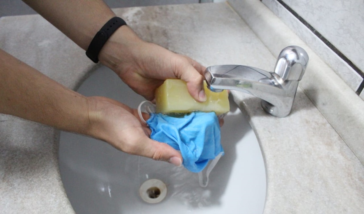 Mãos lavam máscara com sabão em barra na pia